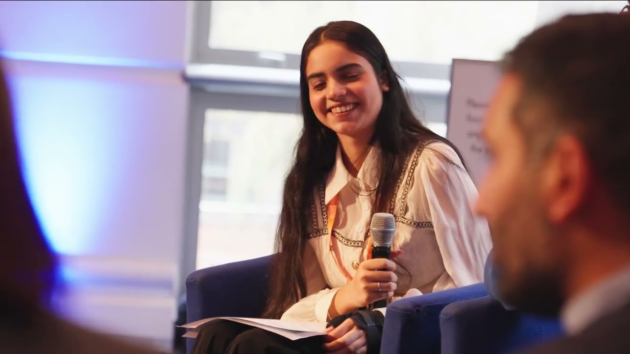 white female student smiling on stage whilst sat down with a microphone
